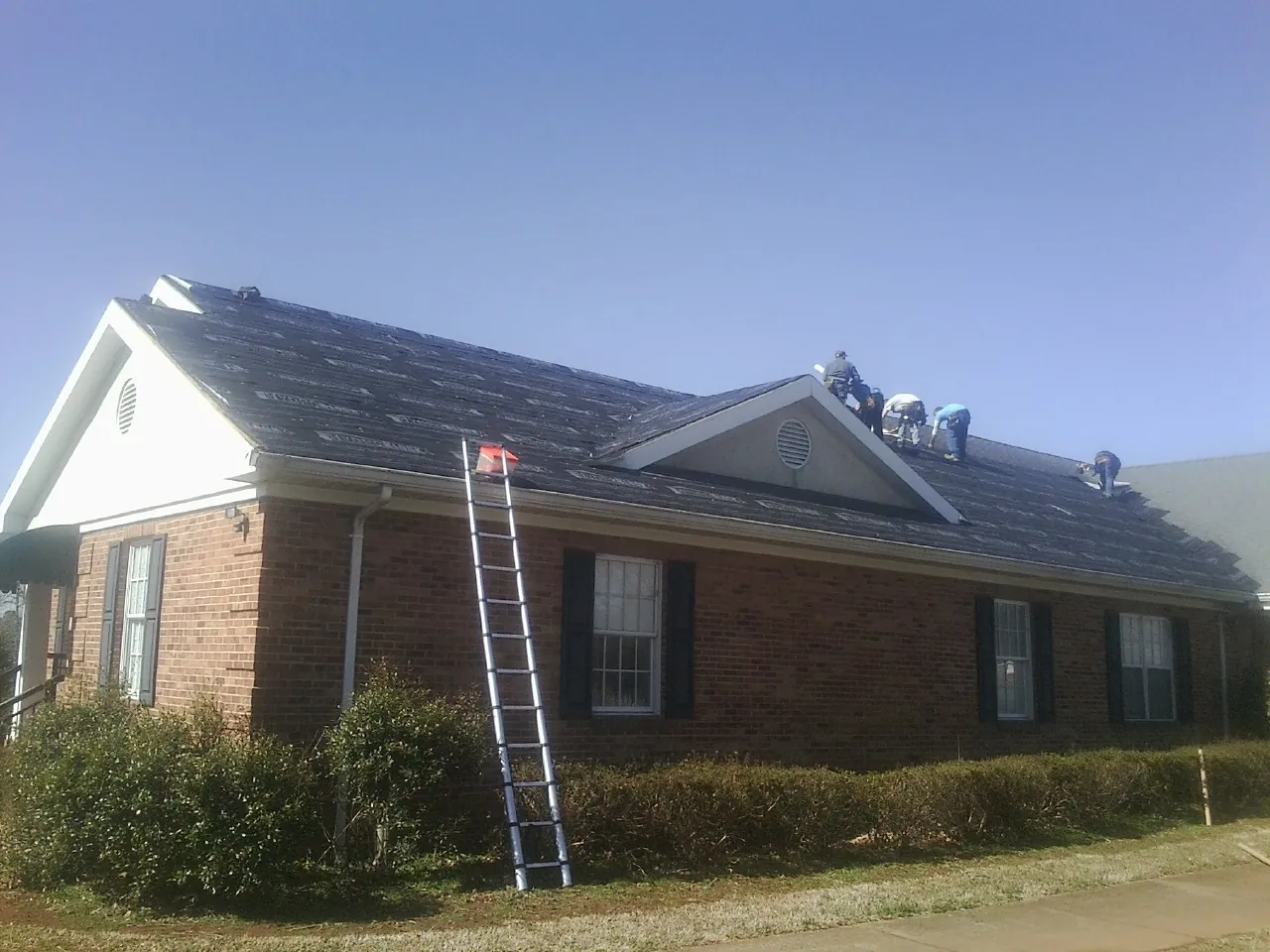 Crew tearing shingles off a brick ranch roof with a ladder set — Emergency Roof Repair work by our crew in Carnation