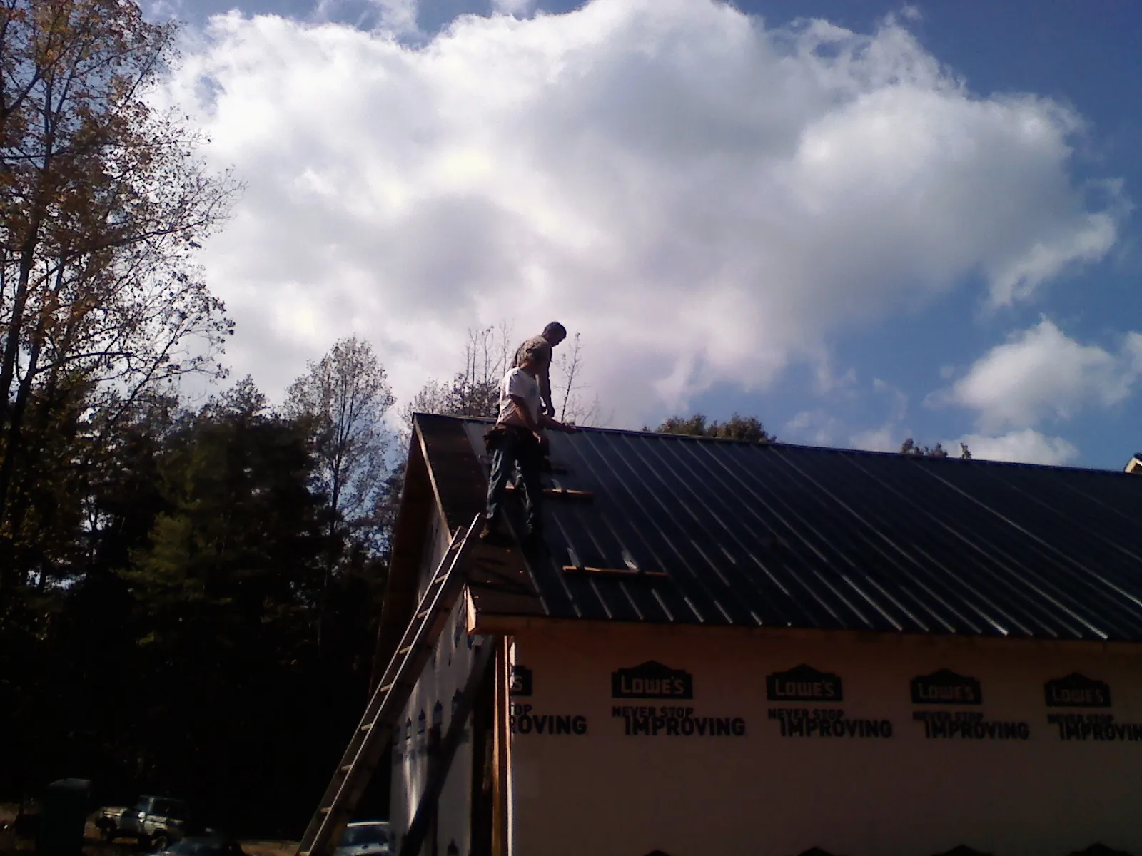 Roofer fastening dark metal panels high against a cloudy sky, from a Roof Inspection job in Carnation