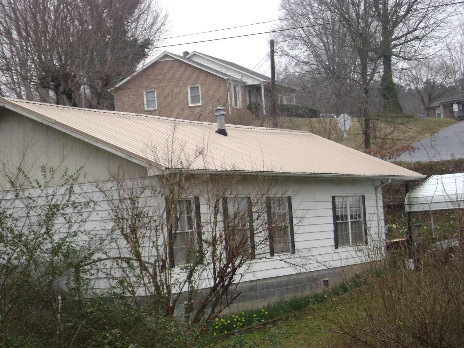 Tan metal roof on a white sided house set into a hillside — Commercial Roofing by Roofing Brothers in Carnation